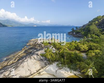Tropischer Strand mit Palmen und Felsen an einer Küste mit klarem blauem Wasser und bewaldeten Hügeln, Blick aus der Vogelperspektive, seychellen, Mahe, Port Glaud und Therese Isla Stockfoto