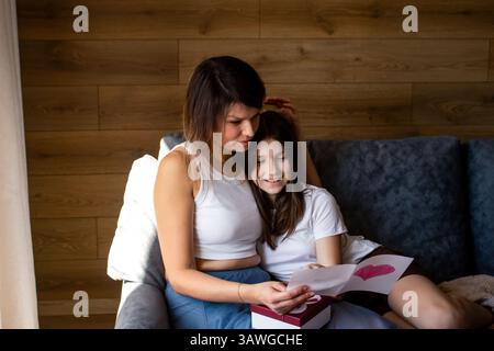 Glücklich lächelnde kaukasische Familie Mutter und Tochter kuscheln, während sie Muttertag, Geburtstag, 8. märz zusammen zu Hause auf Sofa sitzen Stockfoto