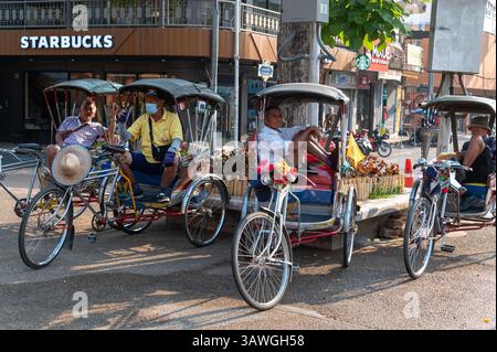 Eine kleine Gruppe von Trischa-Radfahrern wartet auf den Brauch in der Nähe der alten Stadtbefestigung von Chiang Mai im Norden Thailands. Die Rikscha – eine leichte zwei- Stockfoto