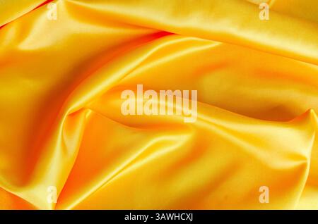 Glänzendes gelbes Satintuch mit strahlenden Oberflächentexturen und feiner gewebter Textur in natürlichen Falten. Stockfoto