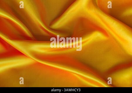 Poliertes goldenes Seidentuch mit seidenem Glanz und wunderschönen Naturdrapierungen. Geeignet für Design und Hintergrundtapeten. Stockfoto