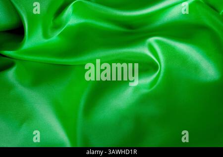 Seidenweiches Satinmaterial in leuchtendem Grün mit eleganten Falten und Glanz. Geeignet für Design und Hintergrundtapeten. Stockfoto