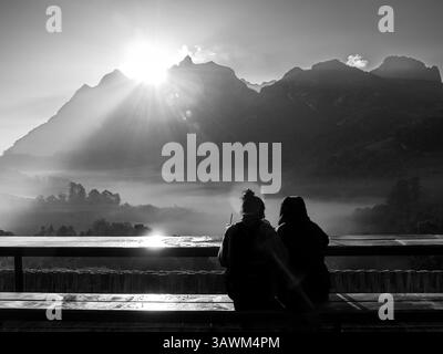 Atemberaubendes Schwarz-weiß-Bild von zwei Touristen, die auf einer langen Holzbank sitzen und sich in das Morgenmeer der Nebelatmosphäre in Doi Luang eintauchen Stockfoto