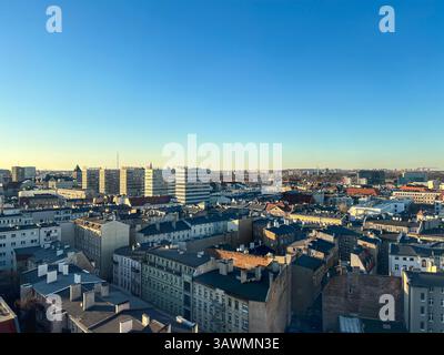 Erhöhter Blick auf eine europäische Stadt mit dicht gepackten Wohndächern und modernen Hochhäusern in der Ferne, aufgenommen an einem klaren Tag Stockfoto