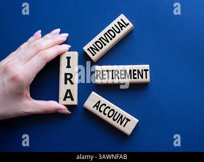 IRA - Symbol für individuelles Abgangskonto. Konzeptwort IRA auf Holzblöcken. Geschäftsmann Hand. Wunderschöner tiefblauer Hintergrund. Business und IRA Konz Stockfoto