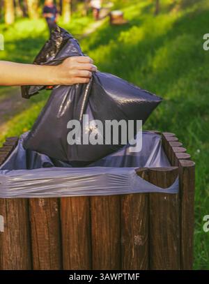 Weibliche Hand wirft Müllsack in Parkkiste Stockfoto