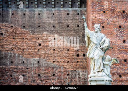 Marmorstatue eines heiligen mit einem Kreuz vor den historischen Backsteinmauern des Castello Sforzesco in Mailand, Italien Stockfoto