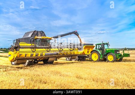 New Holland CR9080 Mähdrescher, der Weizenkorn in Gilibert-Anhänger abgibt, gezogen von John Deere 6620-Traktoren – Zentralfrankreich. Stockfoto