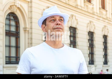 Reifer Mann in weiß, posiert auf einer Straße in der Nähe einer architektonischen Fassade Stockfoto