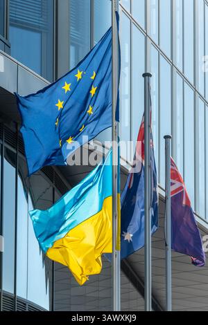 Die Flaggen der Europäischen Union und der Ukraine entwickeln sich im Wind vor dem Hintergrund verglaster Stadtgebäude Stockfoto