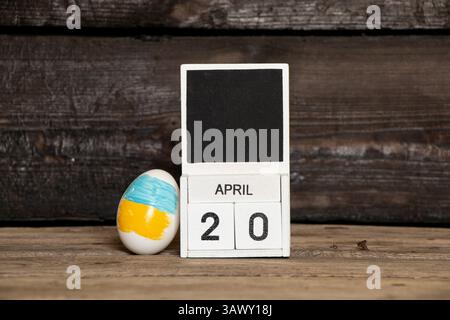 Osterei mit ukrainischer Flagge neben Kalender mit Datum 20. April auf hölzernem Hintergrund, Ostern in der Ukraine Stockfoto