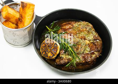 Gegrilltes Rinderrib Eye Steak mit Butter Knoblauch und Rosmarin in einer gusseisernen Pfanne mit weißem Hintergrund Stockfoto
