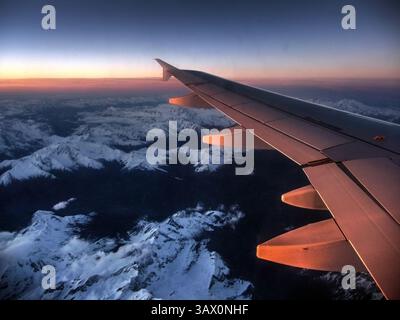 Flugzeugflügel über verschneiten Berggipfeln bei Sonnenuntergang – atemberaubende Aussicht aus der Luft bei einem Höhenflug über die Schweizer Alpen. Stockfoto