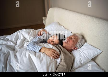 Ruhiges, friedliches, reifes Paar, das sich umarmt in einem gemütlichen Bett im ruhigen Schlafzimmer Stockfoto