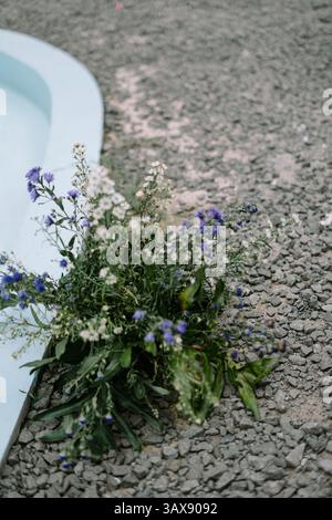 Ein zartes Blumenarrangement liegt am hellen Rand eines Pools und steht im Kontrast zum grauen Kies. Stockfoto