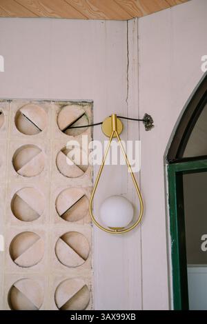 Ästhetische goldene Wandleuchte mit Betonlüftungsblock und Türdetails. Neutrale Töne und geometrische Formen sorgen für eine stilvolle Atmosphäre im Innenraum Stockfoto