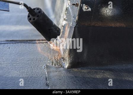 Bauarbeiter, der auf dem Dach schrammt, um mit Gaslämmern zu versiegeln - Nahaufnahme Stockfoto