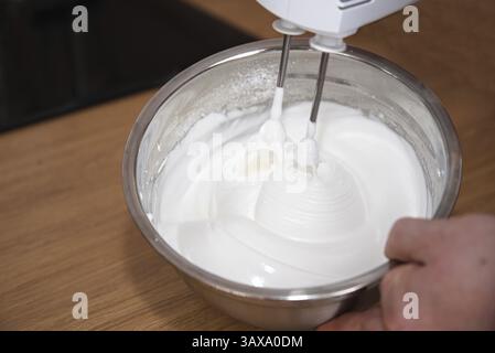 Person in der Küche mit elektrischem Mixer, der Meringue zubereitet - verschlagenes Eiweiß Stockfoto