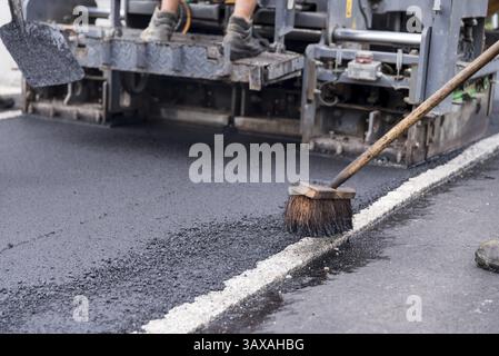 Asphaltieren einer Straße mit einer Baumaschine - Straßenfertiger mit Kehrmaschine Stockfoto