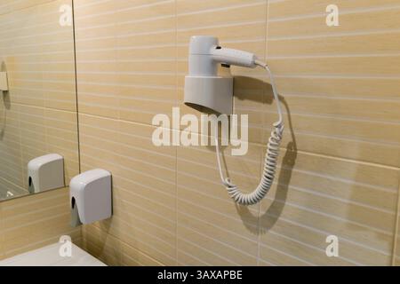 Elektrischer Haartrockner an einem Halter an einer Wand mit Keramikfliesen. Stockfoto