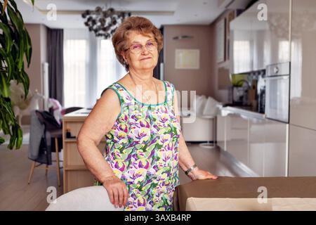 Porträt einer nachdenklichen Seniorin zu Hause, mit Brille und farbenfrohem Sommerkleid, Altern mit würde, Sozialfürsorge, Unabhängigkeit, Ruhestand A Stockfoto