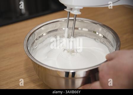 Person, die geschlagenen Eiweiß mit einem Mixer zubereitete - Meringue Stockfoto