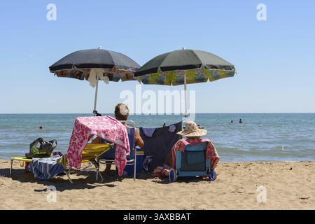 Zwei Badeurlauber genießen ihren Aufenthalt unter dem Sonnenschirm am Sandstrand Stockfoto