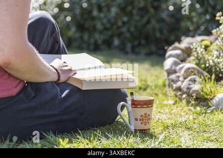 Person, die ein Buch liest, während sie sich im Garten bei einem Kaffee entspannt - entspannend beim Lesen Stockfoto