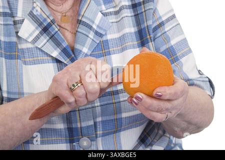 Eine alte Frau schält eine Orange Stockfoto