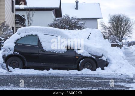 Das geparkte Auto ist beschneit - Beginn des Winters und Schneeräumung Stockfoto