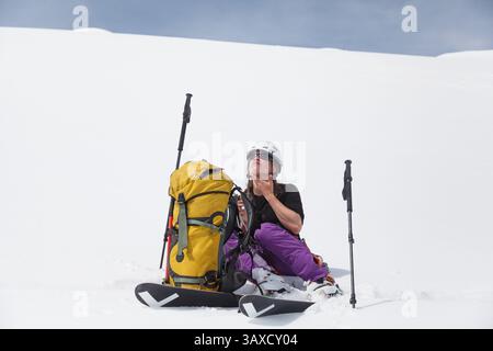 Eine Skilangläuferin sitzt in hellem Schnee, um Sonnencreme aufzutragen Stockfoto