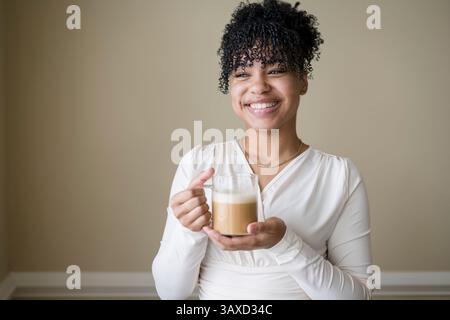 Frau lächelt, während sie Kaffee hält Stockfoto