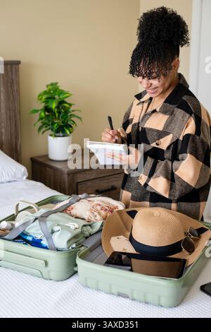 Eine Frau schreibt eine Checkliste, während sie den Koffer für die Reise packt Stockfoto