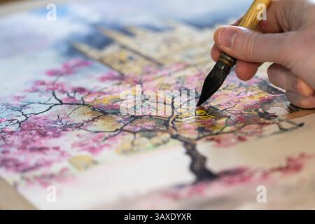 Die Hand eines Mannes hält einen beladenen Pinsel und malte einen Kirschblütenbaum mit Aquarellfarbe, UK. Konzept: Hobbys für Erwachsene, Hobbys für Erwachsene, Künstler Stockfoto