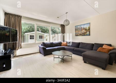 Ein stilvolles, modernes Wohnzimmer mit grauem Sofa, Couchtisch und großen Fenstern, die viel Tageslicht einlassen, schaffen eine warme und einladende Atmosphäre. Stockfoto