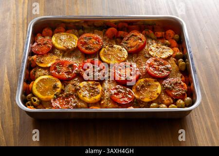 Rohes Fischfilet mit Tomaten, Zitronen, Oliven, Karotten und Kräutern in einer Backform, fertig für den Ofen. Gesunde Mahlzeit vorbereiten. Stockfoto