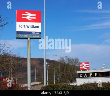 Unverkennbares Doppelpfeil-Symbol der British Rail, das den Standort des Bahnhofs in Fort William markiert, zusammen mit der Beschilderung von Caledonian Sleeper und Scotrail Stockfoto
