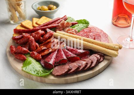 Verschiedene geräucherte Würstchen und andere Snacks serviert mit Wein auf weißem Tisch, Nahaufnahme Stockfoto
