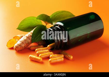 Kurkuma-Rhizome, Kapseln und umgedrehte medizinische Flasche auf orangem Hintergrund, Nahaufnahme Stockfoto