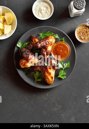 Gegrillte Hähnchenflügel auf Teller über dunklem Steinhintergrund. Leckeres gegrilltes Hähnchenfleisch zum Abendessen. Draufsicht, flach Stockfoto