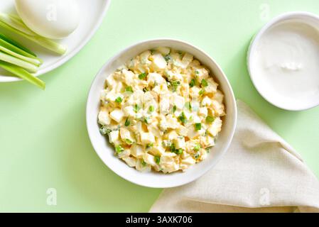 Köstlicher Eiersalat mit grünen Zwiebeln und Joghurtdressing in Schüssel auf grünem Hintergrund. Draufsicht, flach Stockfoto