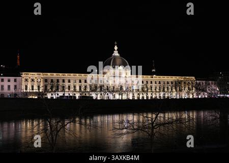 Die beleuchtete Fassade des Grand Hotel-Dieu in Lyon, Frankreich, spiegelt sich nachts wunderschön im ruhigen Wasser der Rhone wider. Stockfoto