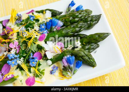 Grüner Spargel mit Safransauce und essbaren Blüten auf einem Teller. Stockfoto