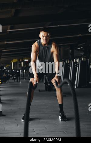 Vertikales Foto des großen Körpers eines Sportmannes, der mit schweren Kampfseilen im Fitnessstudio trainiert Stockfoto