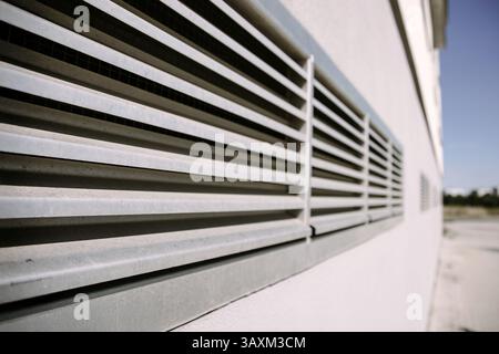 Ein Lüftungsgitter aus Metall, das an der Wand eines modernen Industriegebäudes montiert ist. Hervorragend geeignet für die Veranschaulichung von Konzepten der Luftströmung, HLK-Systeme und Konstruktion Stockfoto