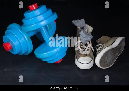 Auf dem zerkratzten Gummiboden eines leeren Fitnessstudios liegen blaue Kurzhanteln und abgenutzte Sneakers mit alten Socken. Stockfoto