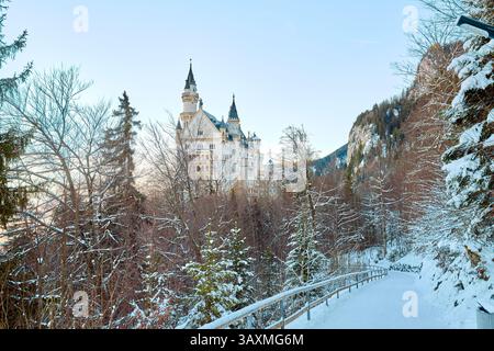 Blick auf die schneebedeckte Berglandschaft mit Schloss Neuschwanstein im Hintergrund, das frühmorgendliche Licht in einer ruhigen Winterszene einfängt und das zeigt Stockfoto