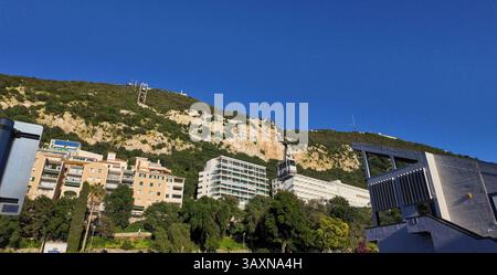 Seilbahn auf dem Felsen von Gibraltar, die Touristen auf den Gipfel bringt, vorbei an Gebäuden und üppiger Vegetation unter einem klaren blauen Himmel - GIBRALTAR, Großbritannien Stockfoto