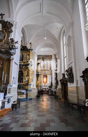 Grodno, Weißrussland, 03.01.2025 Ein langer, schmaler Raum mit hoher Decke und weißen Wänden. Der Raum ist mit Holzbänken und ein paar Bänken gefüllt. Die Bänke A Stockfoto