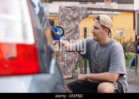 Ein junger Mann, der sein Auto zu Hause draußen putzt Stockfoto